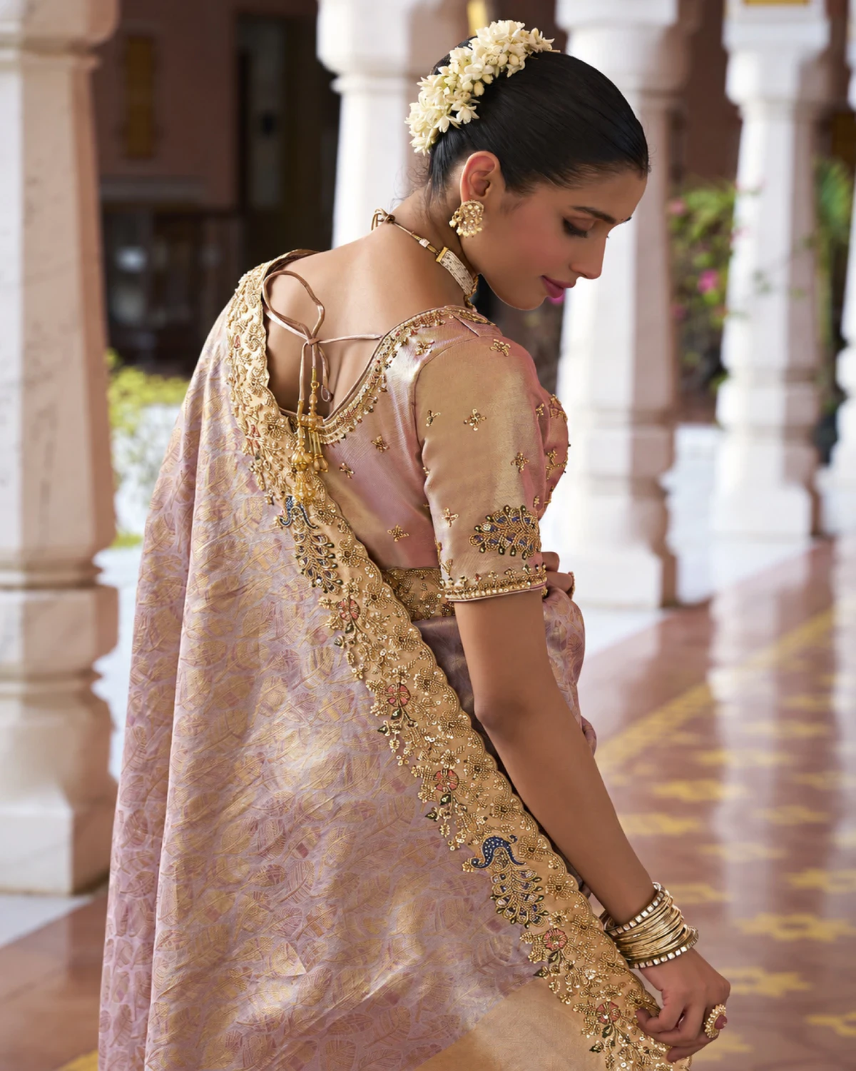 Back view of a woman in the dusty lilac soft silk saree, showing its beaded border and the blouse's tie-up back