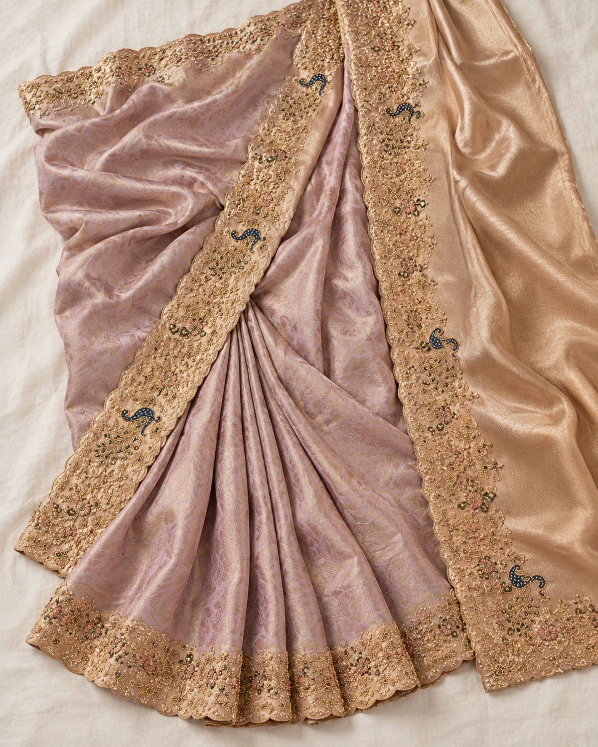 The dusty lilac soft silk saree laid flat on a cream cloth, showing its peacock border and wide gold pallu