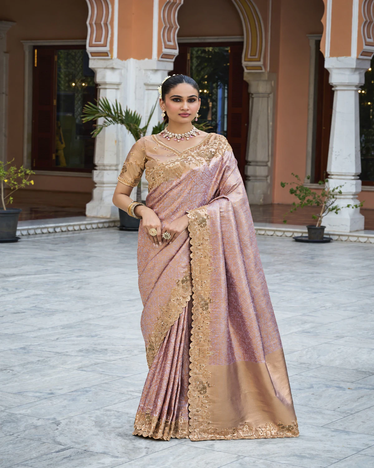 Woman wearing the blush lilac soft silk saree with its elephant border, standing in a marble courtyard