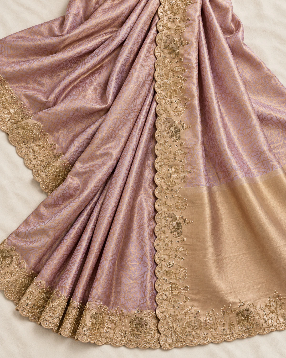 The blush lilac soft silk saree laid flat on a cream cloth, showing its gold lattice, elephant border and gold pallu end