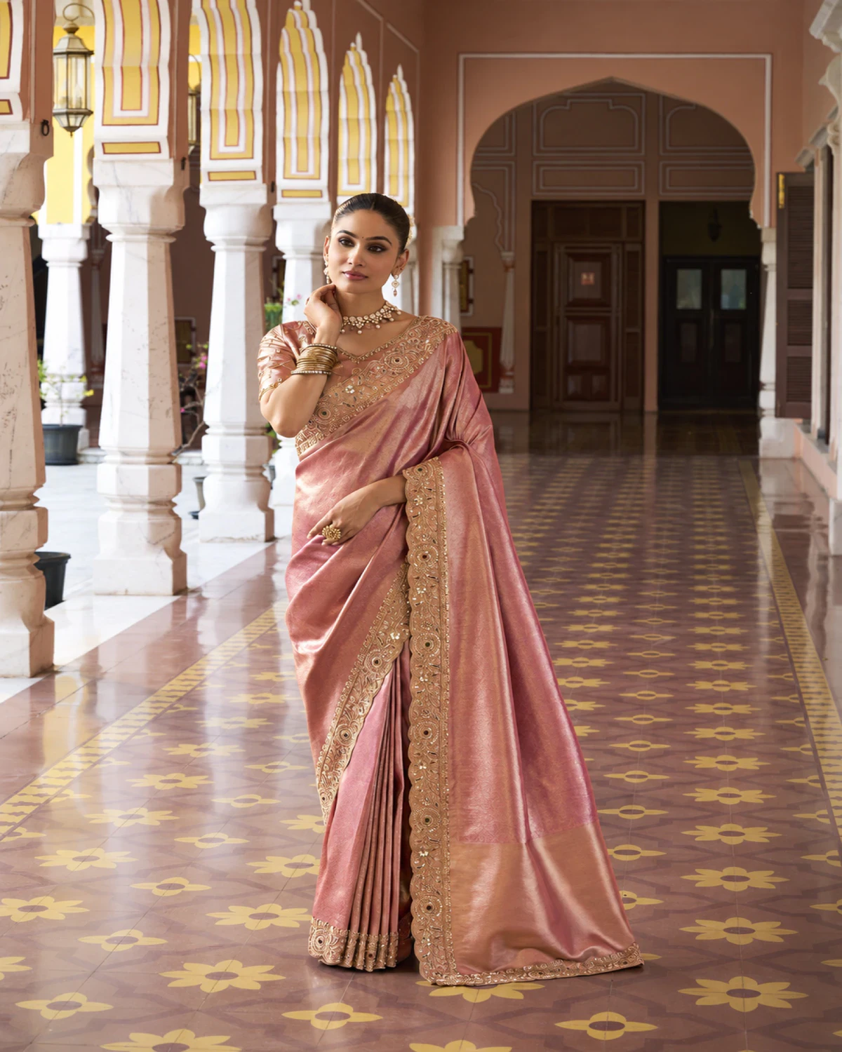 Woman wearing a rose coral Kanjivaram-style soft silk saree with a beaded roundel border, in an arched courtyard