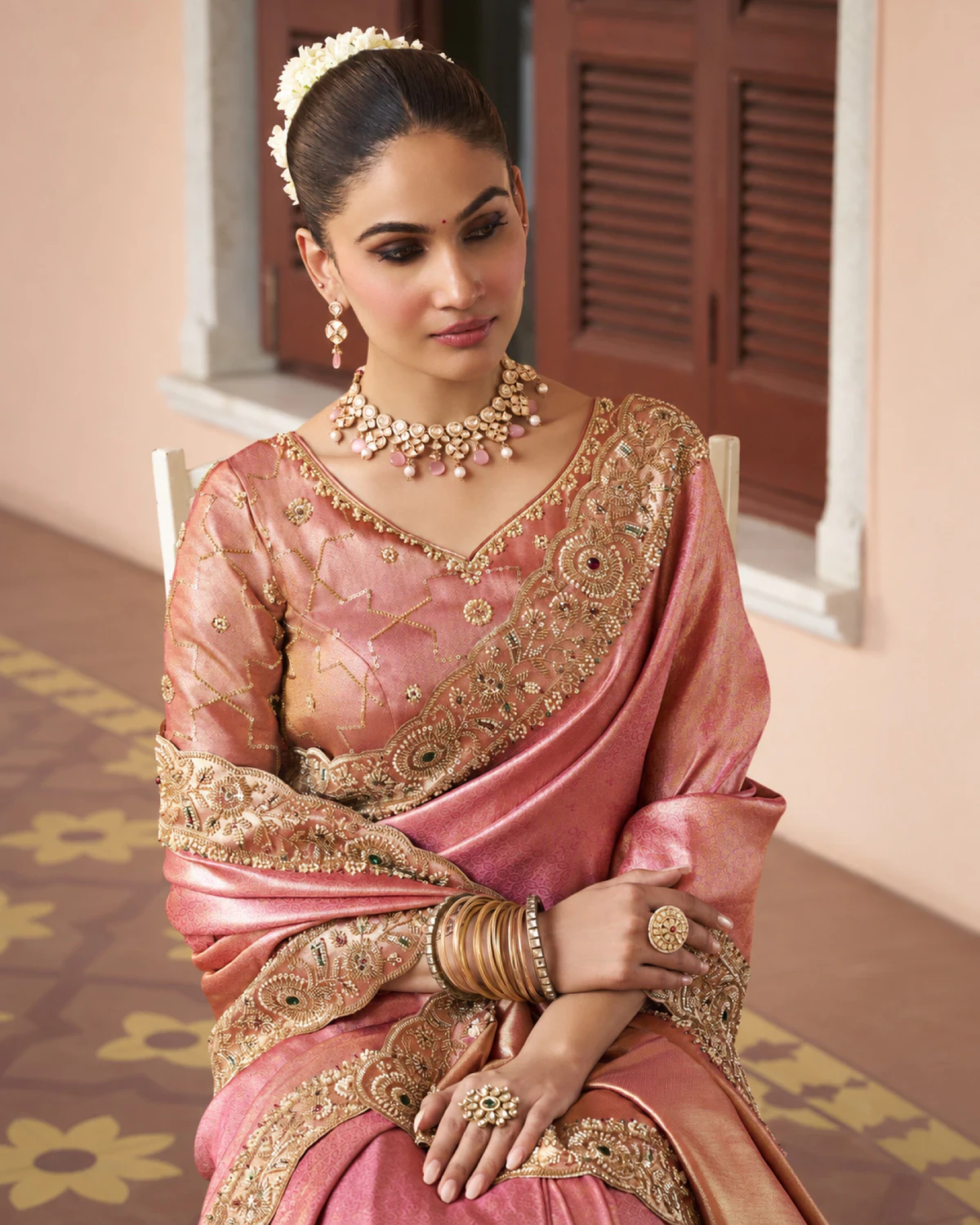 Woman seated in the rose coral soft silk saree, showing its beaded border and pink-gold blouse