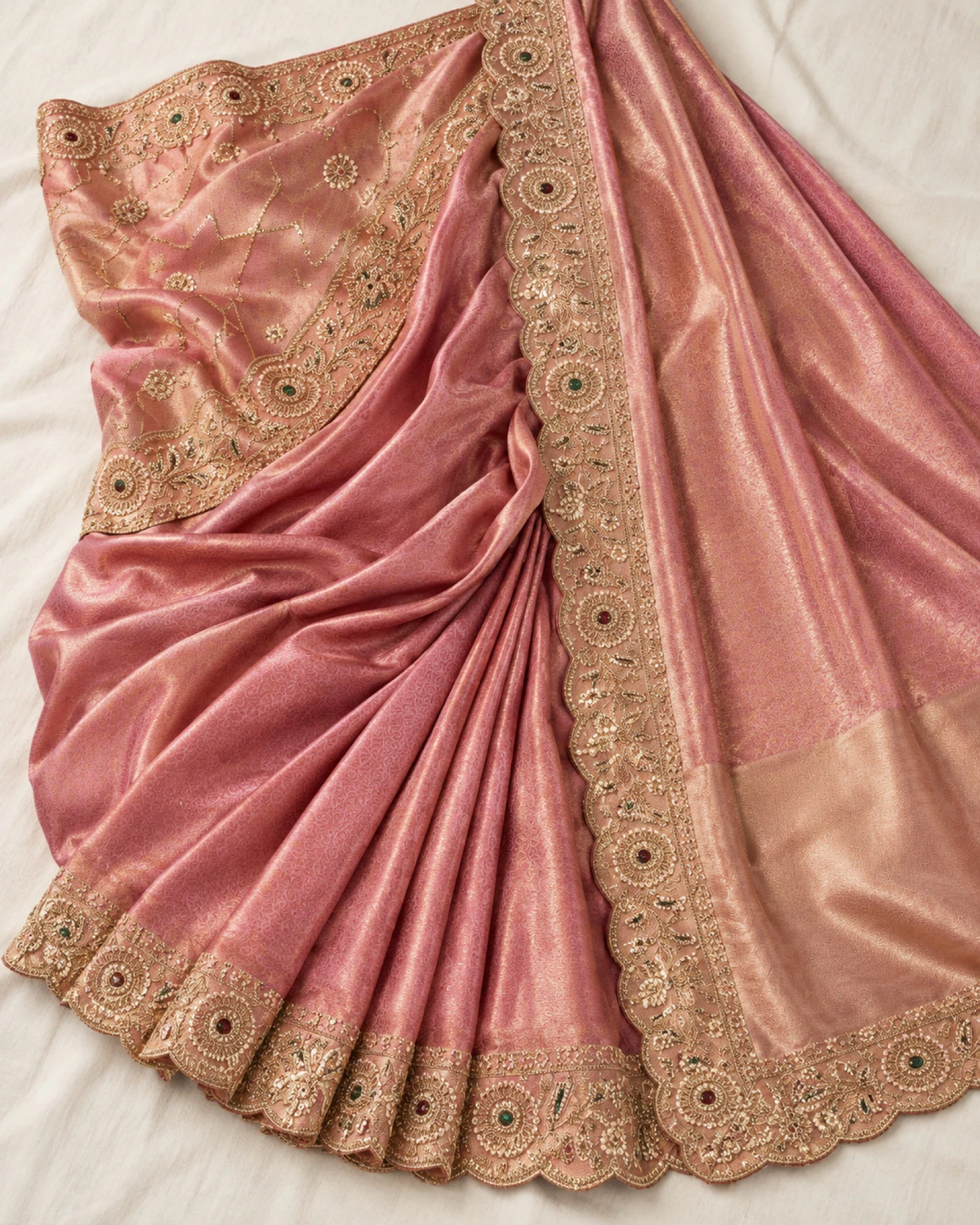 The rose coral soft silk saree laid flat on a cream cloth, showing its shimmering body and roundel border