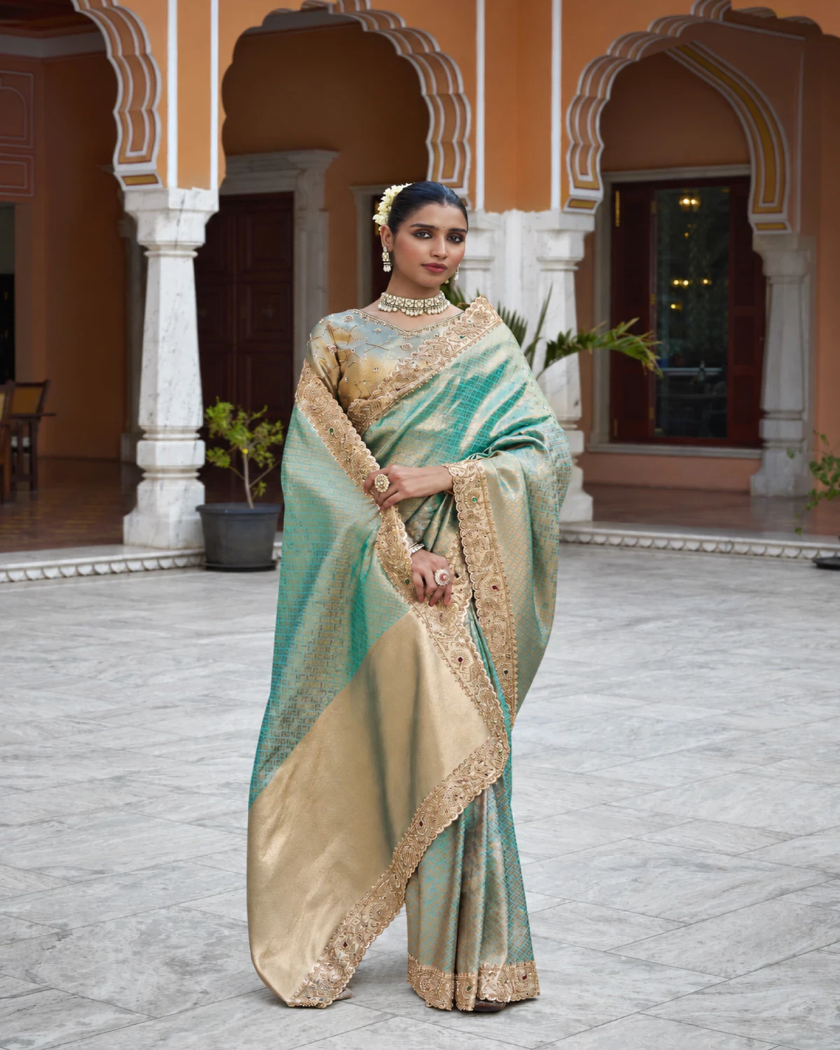 Woman wearing the mint green soft silk saree with its wide gold pallu held open, in a marble courtyard