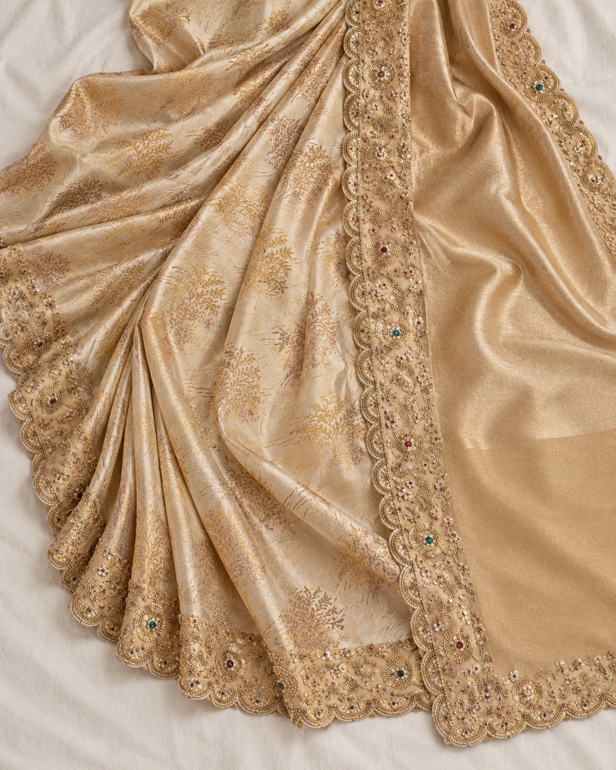 The ivory soft silk saree laid flat on a cream cloth, showing its woven gold trees, beaded border and gold pallu